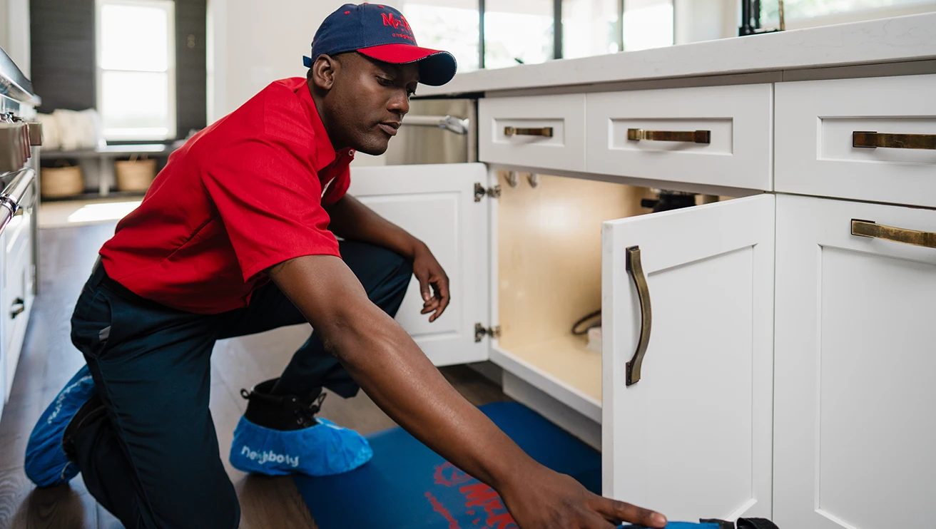 Mr. Rooter technician working under a kitchen sink to clear a clogged drain.