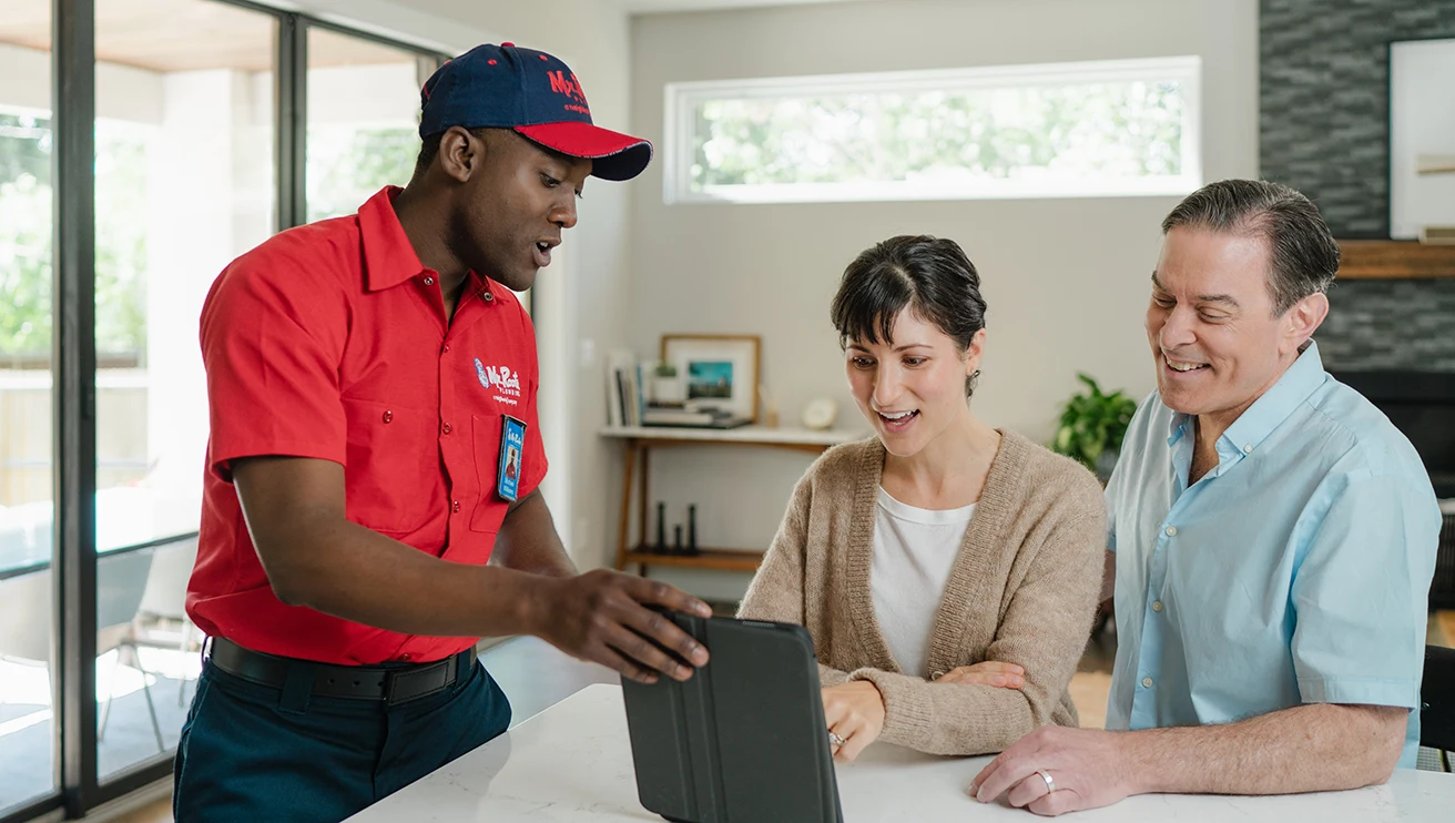 Mr. Rooter technician showing two customers a service plan on a tablet.