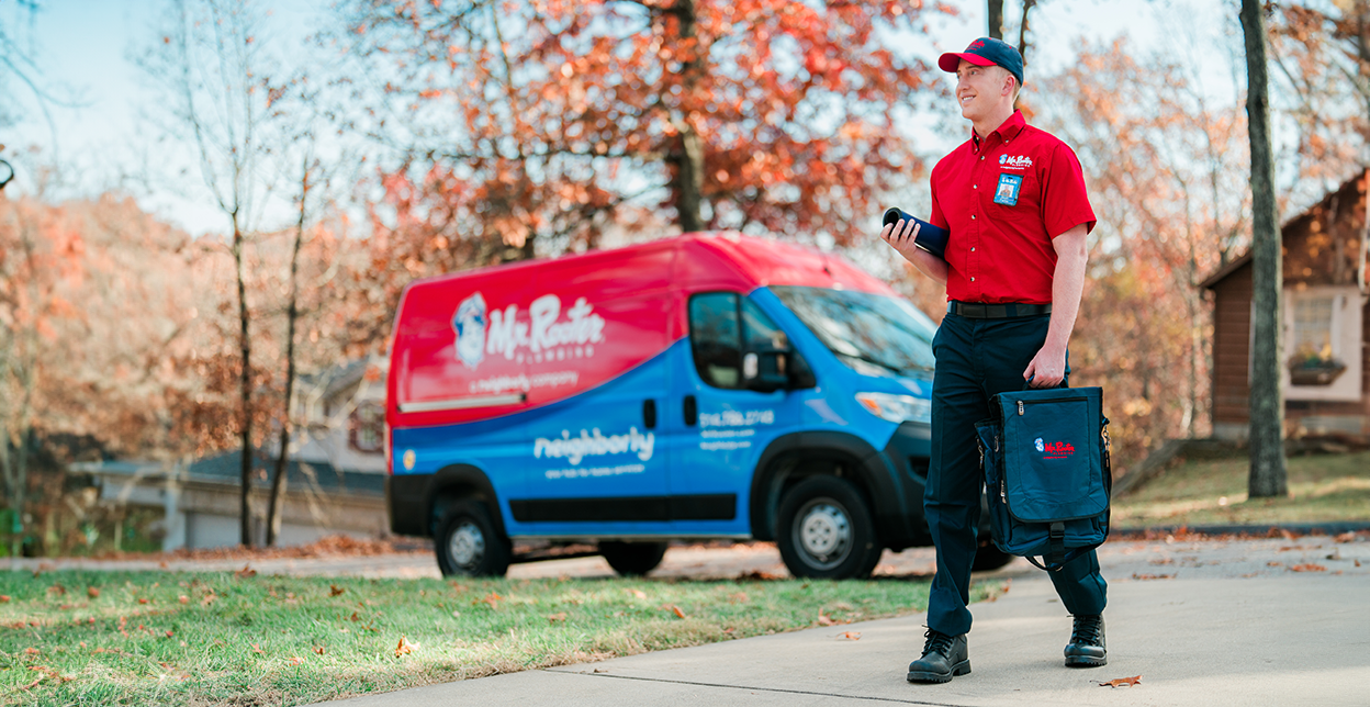 Mr. Rooter techniican walking up to a customer's home with a branded van parked in the background.