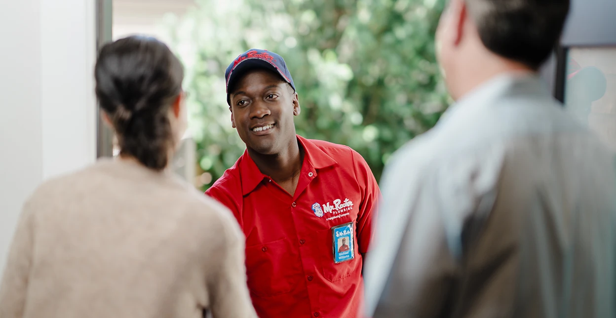 Two customers greeting a Mr. Rooter technician at their front door.