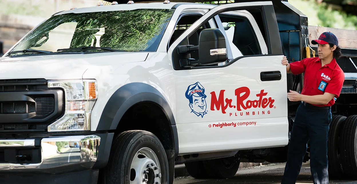 White Mr. Rooter truck parked with technician standing beside it.