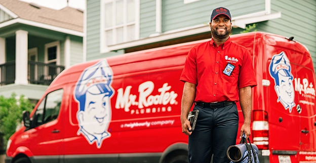 Mr. Rooter professional walking up to a customer's home with a branded van parked in the background.