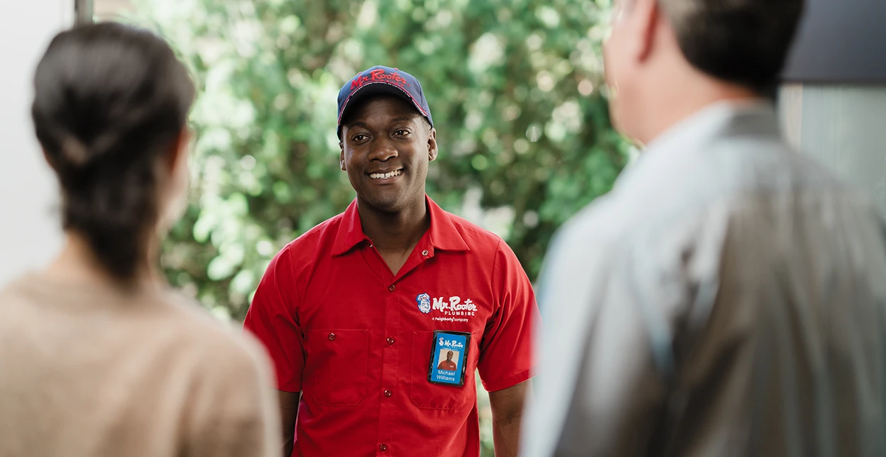 Smiling Mr. Rooter technician greeting two customers at their home's front door.