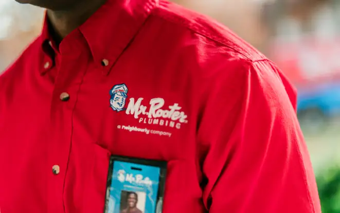 The Mr. Rooter logo on the red polo shirt of a technician.