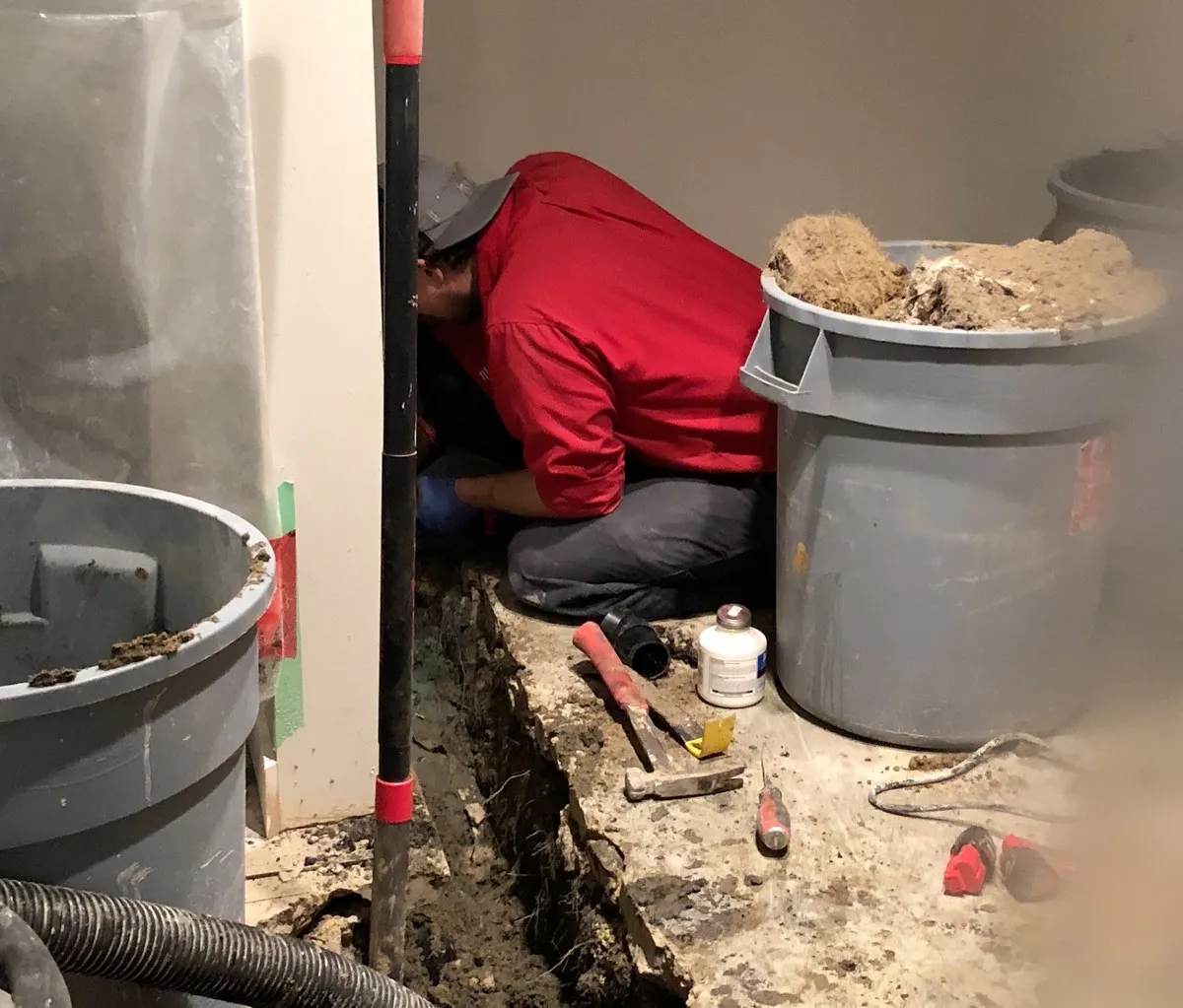 A plumber from Mr. Rooter Plumbing working on a pipe inside of a trench that&rsquo;s been dug through the concrete foundation of a home inside the home&rsquo;s basement.