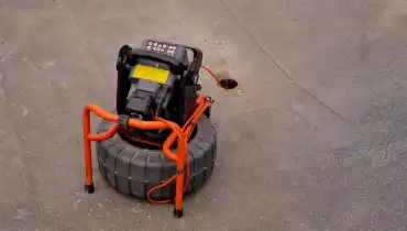 Sewer scope equipment is being used to inspect a pipe through a small opening on a concrete surface.