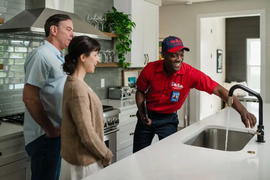 Mr. Rooter Plumbing&reg; professional showing homeowners how he repaired their leaky kitchen faucet.