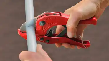 A plumber using a pair of pipe cutters to cut a length of grey pipe while repiping a home in Calgary, AB with Poly B pipes.