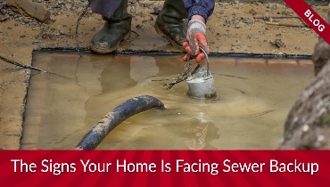 A sewer drain overflowing with water and a plumber crouched down next to it using tools to unclog it.