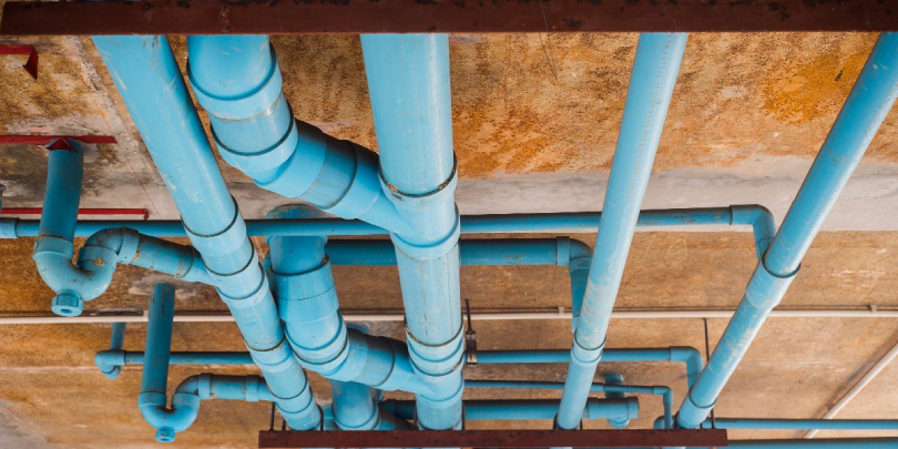 Blue PVC pipes of various sizes running along the ceiling of a building.