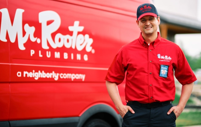 Mr. Rooter technician standing by a red branded van.